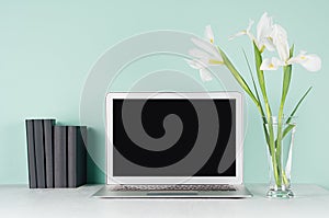 Back to school background - workplace with blank notebook monitor, black books and white fresh flowers in light green mint menthe.