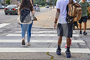 Back to school - the backs of college students crossing urban crosswalk with backpacks - ethnic diversity and casual dress with ca