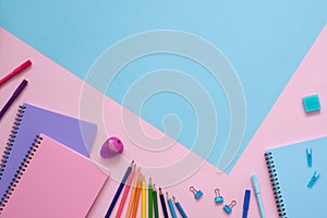 Blue, purple and pink notebooks, color pencils, felt tip pens, pencil sharpener, eraser and paper clips on the pink background