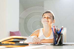 Back to school. Boy with broken arm in gypsum writing, drawing in notebook sitting at desk and doing homework.