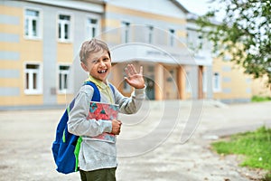 Back to school. A boy from an elementary school in the school yard waves