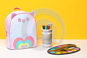 Back to school. Colourful school equipment and a bright school backpack on white table in front of an yellow  background. Concept