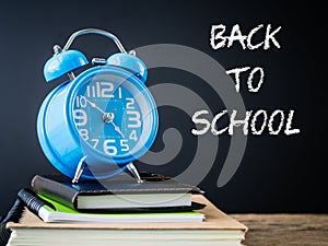 Alarm clock on stacks of books on wooden table and black background.