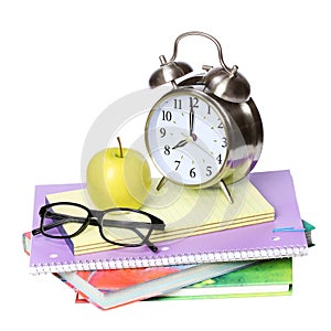 Back to school concept. An apple, alarm clock and glasses on pile of books isolated on white