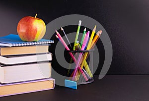 Back to school concept. Apple, books and school supplies painted over on a black board background. Copy space.