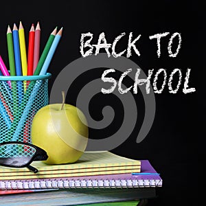 Back to school concept. An apple, colored pencils and glasses on pile of books over black background