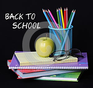 Back to school concept. An apple, colored pencils and glasses on pile of books over black background
