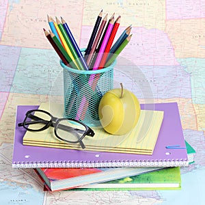 Back to school concept. An apple, colored pencils and glasses on pile of books over map