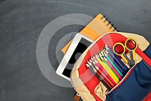 Back to school concept. Backpack with school supplies, tablet and against chalk board. Top view. Copy space