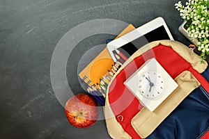 Back to school concept. Backpack with school supplies, clock, tablet and apple against chalk board. Top view. Copy space