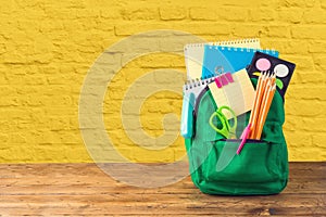 Back to school concept with bag backpack and school supplies on wooden table over yellow brick wall background photo
