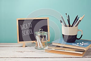 Back to school concept with books, pencils in cup and chalkboard on wooden white table