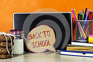 Back to school concept - chat bubble and blackboard with pencil-box and books, notebook and sticky note, milk and cookies