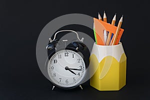 back to school concept. Close up image of school supplies and round clock are on black background.