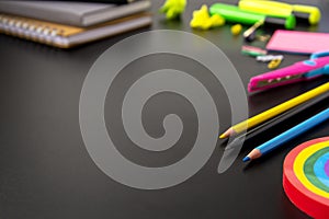 Back to school concept. Colorful pencils, rainbow eraser, notebook, sticky notes and office supplies on black background