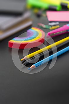 Back to school concept. Colorful pencils, rainbow eraser, notebook, sticky notes and office supplies on black background