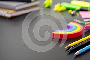 Back to school concept. Colorful pencils, rainbow eraser, notebook, sticky notes and office supplies on black background. Copy