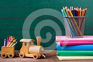 Back to school concept, coloured pencils, wax crayons and books with toy train on empty chalkboard background