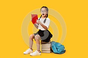 Cute School Girl Reading Book Sitting On Books, Yellow Background