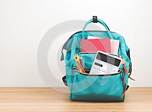 Front view of green backpack with school supplies on wooden table and white background with copy space