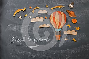 Back to school concept. Hot air balloon, space elements shapes cut from paper and painted over classroom blackboard background.