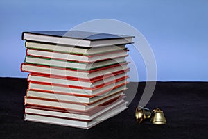 Back to school concept. A large pile of books and a bell side view on a blue background. With place for text