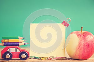 Back to school concept. Miniature Red Car Carrying a colorful pencils and red apple on wooden table. Toning image