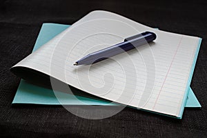 Back to school concept. Notebook with notice paper and pen on black background