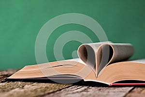 Back to school concept, open book and pages folded in the shape of a heart on an old wooden surface on a backdrop of clean green