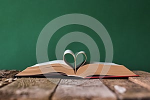 Back to school concept, open book and pages folded in the shape of a heart on an old wooden surface on a backdrop of clean green