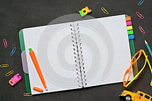 Back to School concept - open copy book with office and student supplies on black chalk background. Space for text