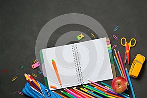 Back to School concept - open copy book with office and student supplies on black chalk background. Space for text