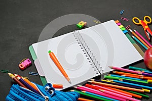 Back to School concept - open copy book with office and student supplies on black chalk background. Space for text