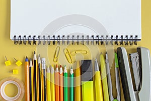 Back to school concept. Open empty mockup notebook and colored school stationery. Yellow paper background. Flat lay, top view,