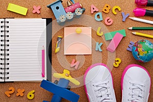 Back to school. Concept with pencils, letters, numbers and sneakers on a cork background. Opened notepad and globe. View from