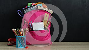 Back to school concept. pink backpack and school supplies on the desk at the blackboard. copy space.