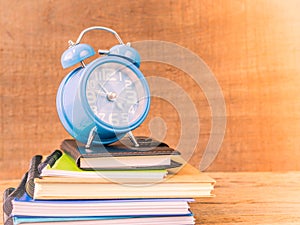 Retro style of alarm clock on stacks of books with wooden table background.