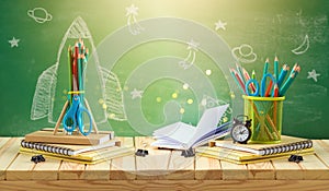 Back to school concept with rocket sketch, pencils and notebook on wooden table over chalkboard background