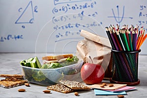 Back to School concept, school supplies, biscuits, packed lunch and lunchbox over white chalkboard, selective focus.