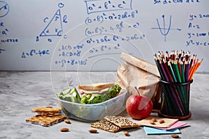 Back to School concept, school supplies, biscuits, packed lunch and lunchbox over white chalkboard, selective focus.