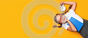 Back to school concept. Shocked pupil with an alarm clock and a book on a yellow background. Top view banner