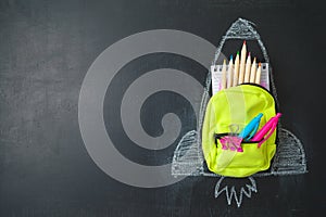 Back to school concept with small bag backpack, school supplies and rocket sketch over chalkboad background