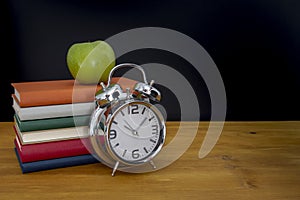 Back to school background with books and alarm clock over chalkboard