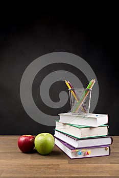 Back to School Concept, Stacked books, Coloring Pencils and red and green apple isolated on black blackboard background