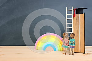 Back to school concept. Top view image of two kids standing next to ladder and book over wooden desk