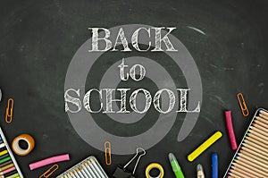 Back to school concept. Top view tationery, notepads, pencils and clips over classroom blackboard with white chalk sign