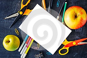 Back to school concept. White blank sheet isolated with two apples and school supplies on table top view