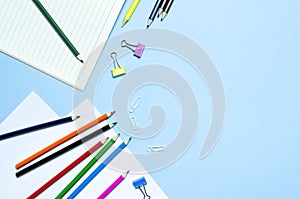 Back to school concept. Wooden colored pencils, clean school notebook in line, paper clips on blue background top view flat lay