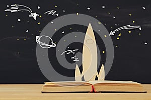 Back to school concept. wooden rocket and space sketchs over open book in front of classroom blackboard. photo