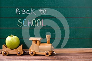 Back to school concept, wooden toy train carrying a green apple on chalkboard background